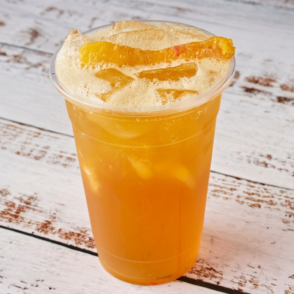 Orange sparkling beverage with ice and frothy citrus garnish in a clear plastic cup on a distressed white wooden table.