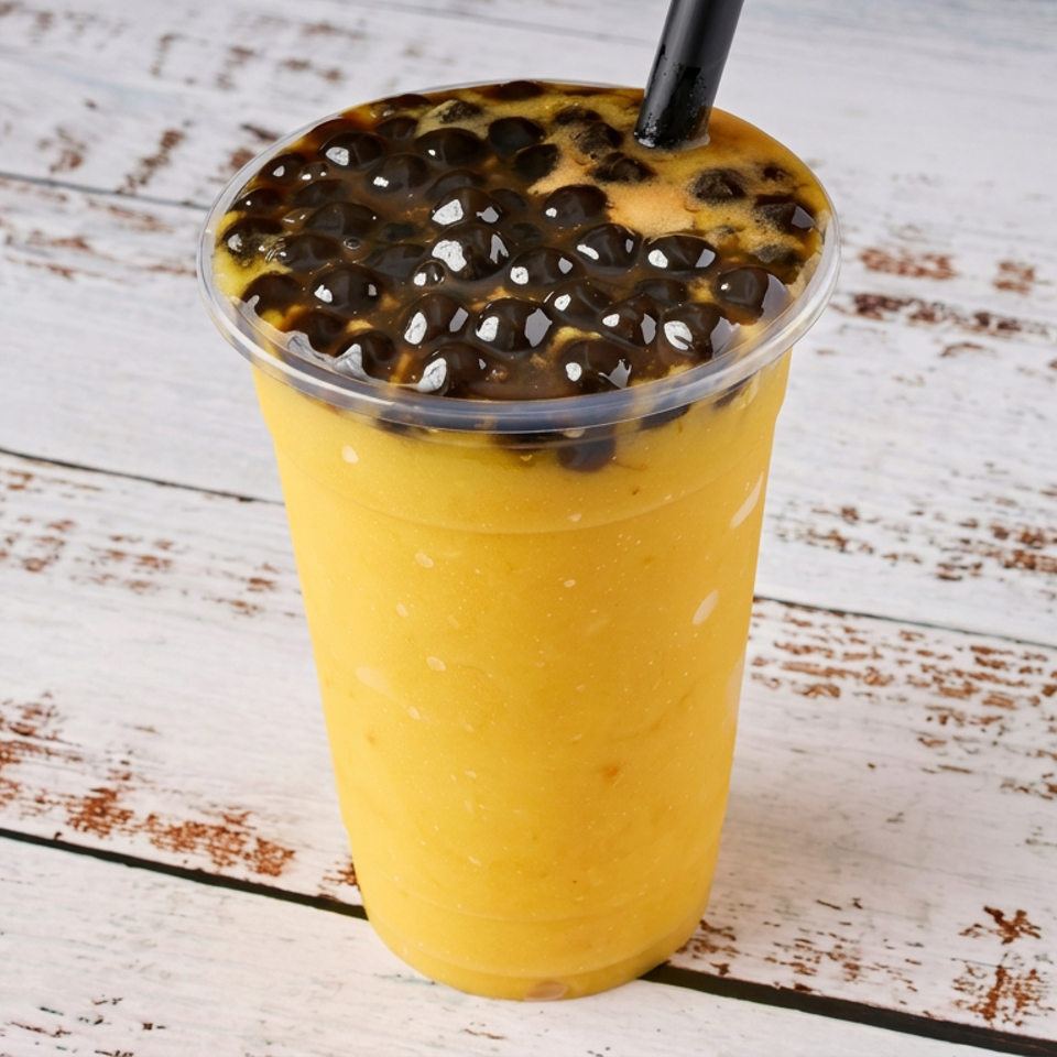 Bright yellow fruit drink topped with dark tapioca pearls in a clear cup on a rustic white wooden table.